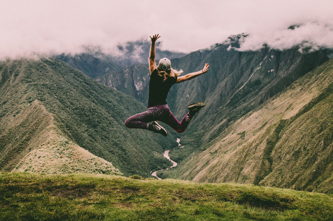 sporty woman jumping into air in front of a mountain valley